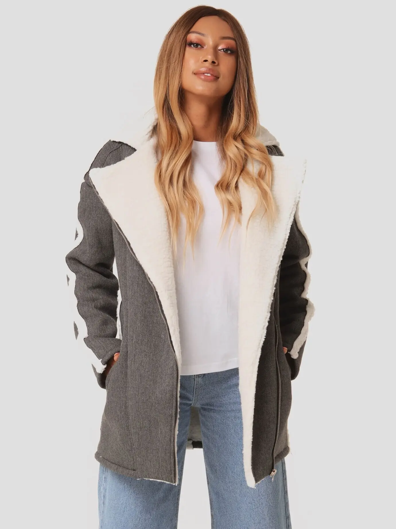 Dieses hübsche Mädchen trägt eine graue Jacke, darunter ein weißes T-Shirt und moderne Jeans. Junge Hipster-Frau im lässigen Look.